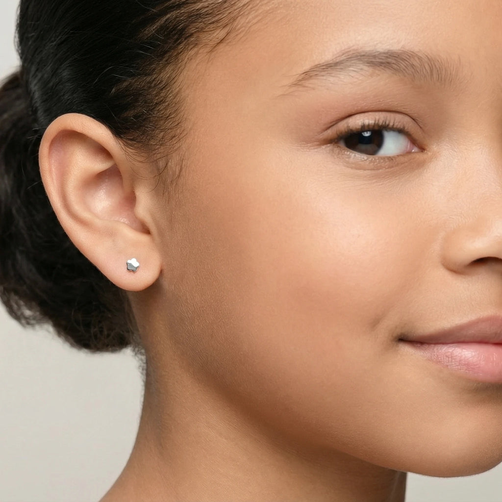 Closeup of a girl wearing a silver flower stud earring on a plain background