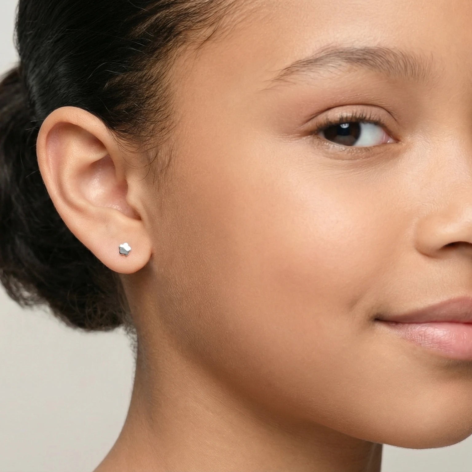 Closeup of a girl wearing a silver flower stud earring on a plain background