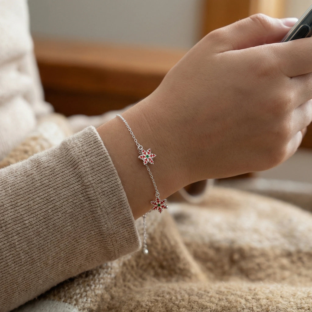 Closeup of a girl's hand wearing a silver bracelet with red and green snowflake charms, holding a phone.