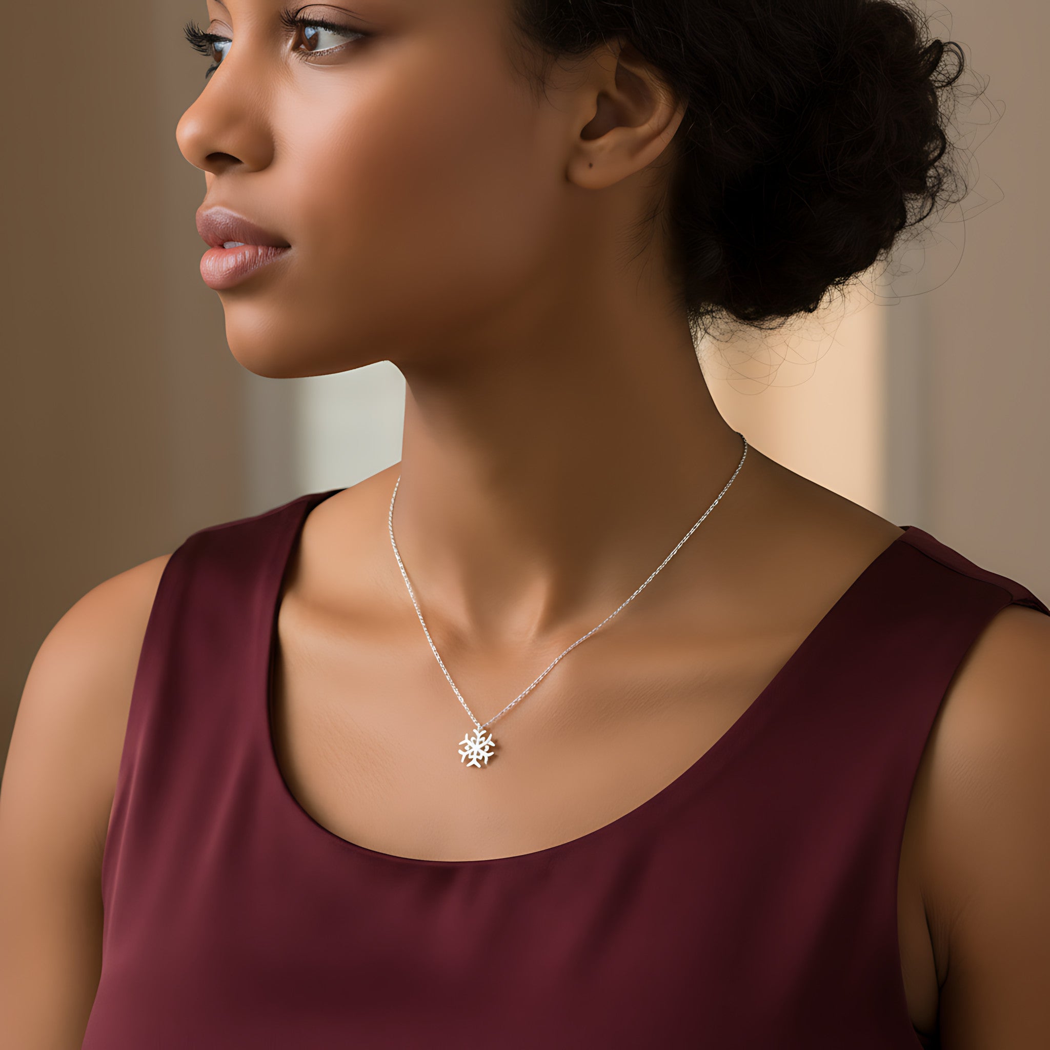 Closeup of a female wearing a silver necklace with a small snowflake pendant against a neutral background