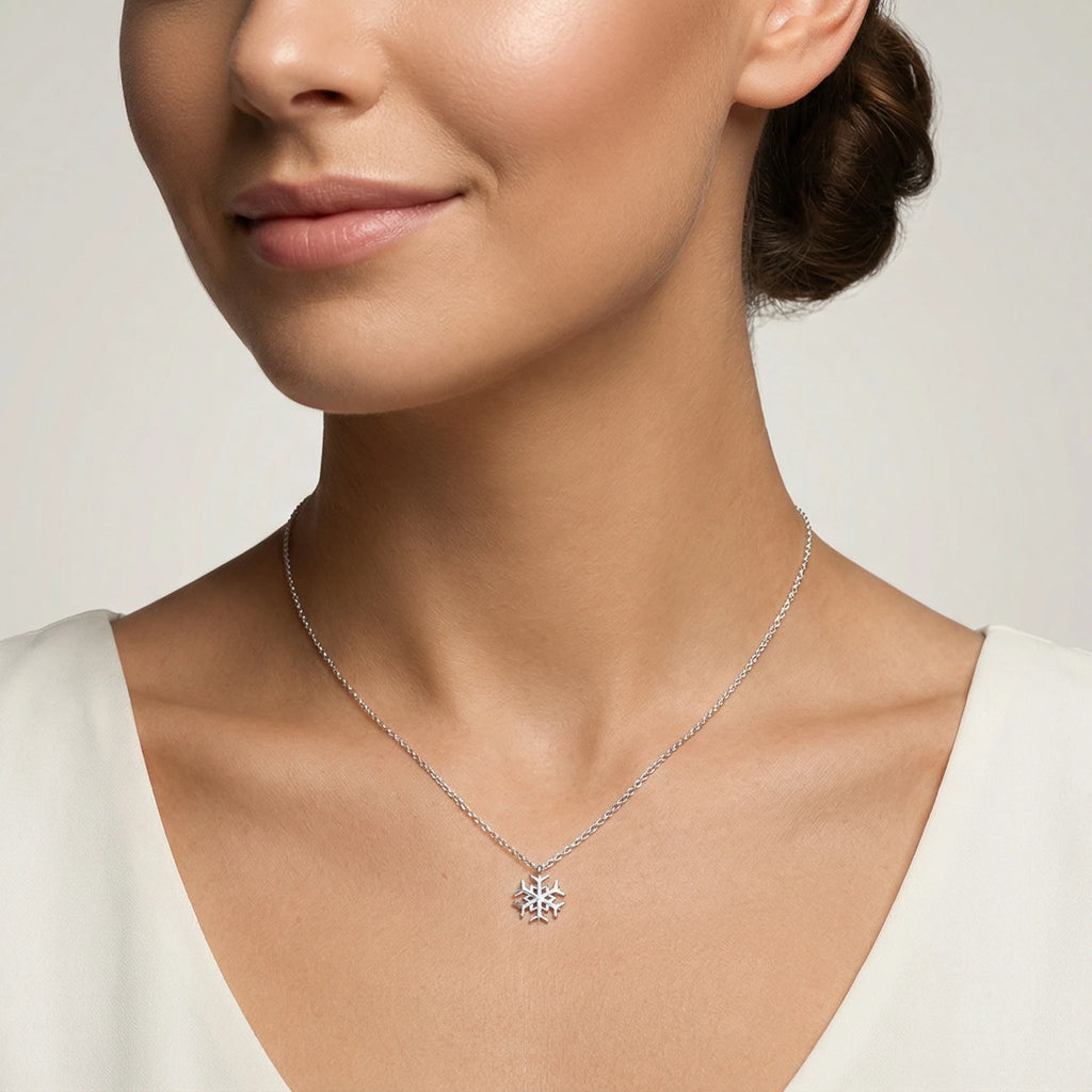 Closeup of a female wearing a silver necklace with a small snowflake pendant against a neutral background