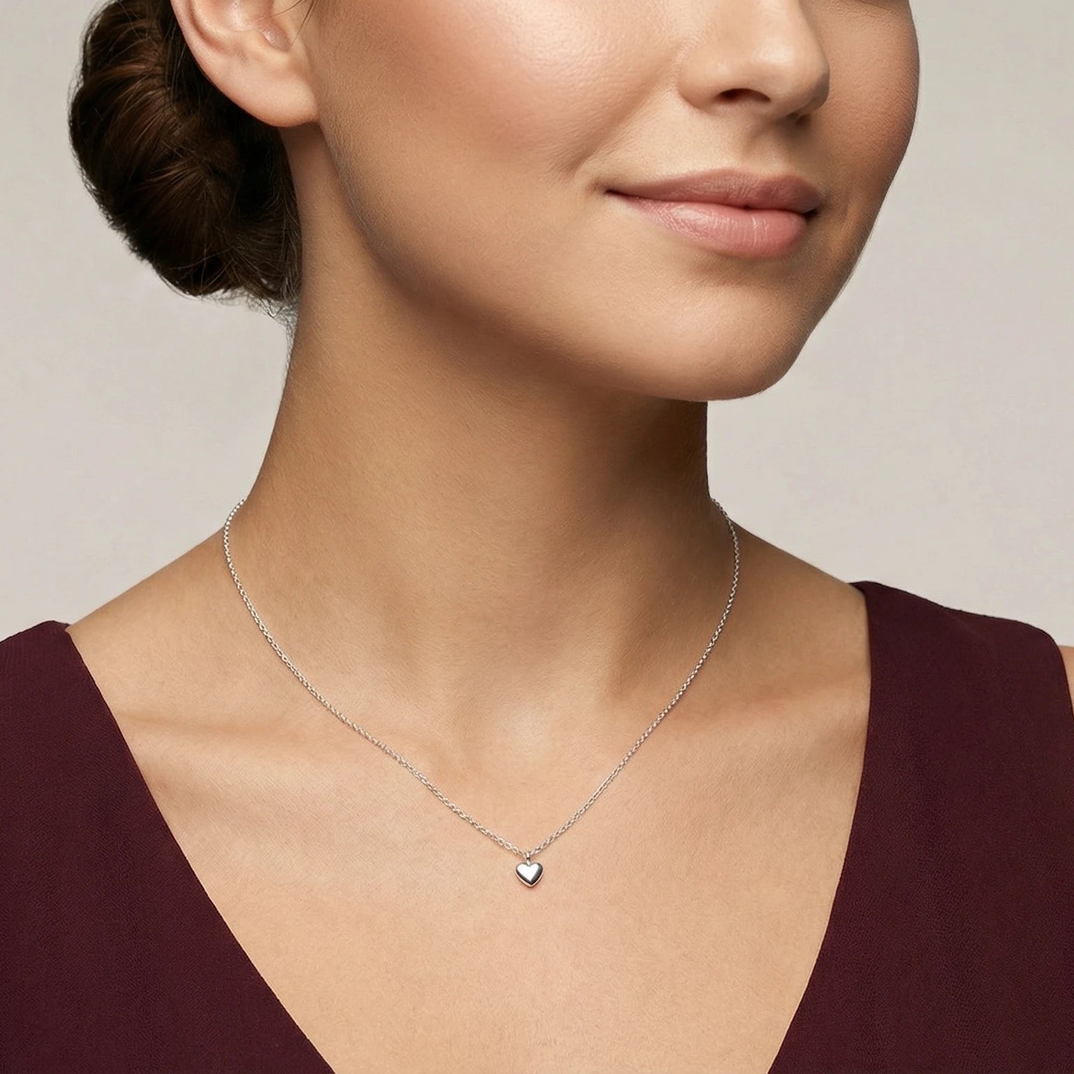 Woman wearing a delicate heart pendant necklace against a neutral background