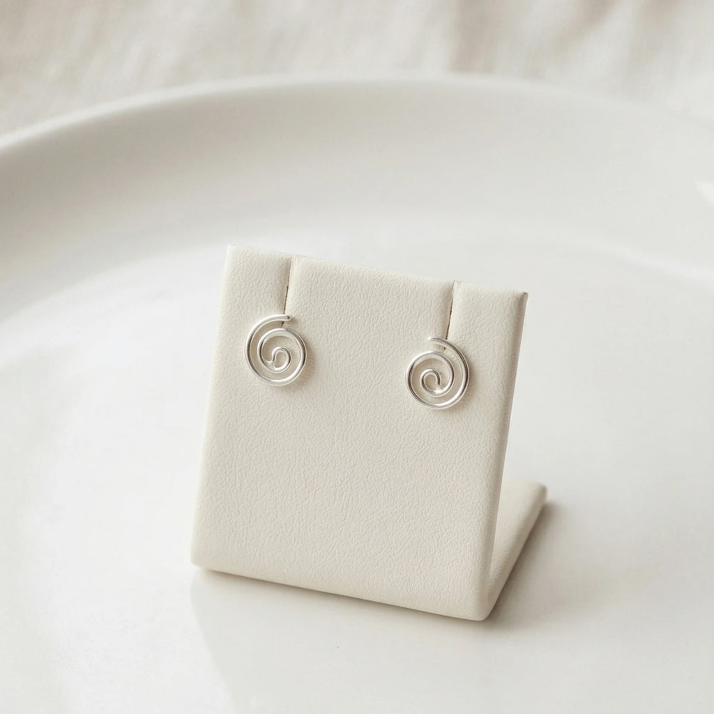 Silver spiral stud earrings on a white jewelry display stand with a white background