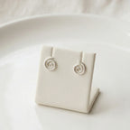 Silver spiral stud earrings on a white jewelry display stand with a white background