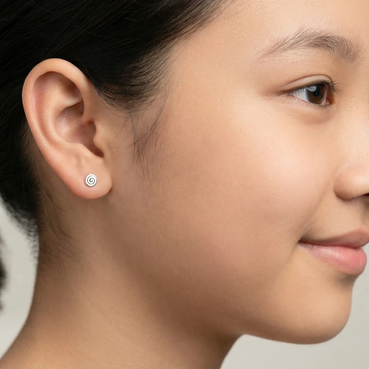 Closeup of a girl wearing a silver spiral stud earring on a blurred background