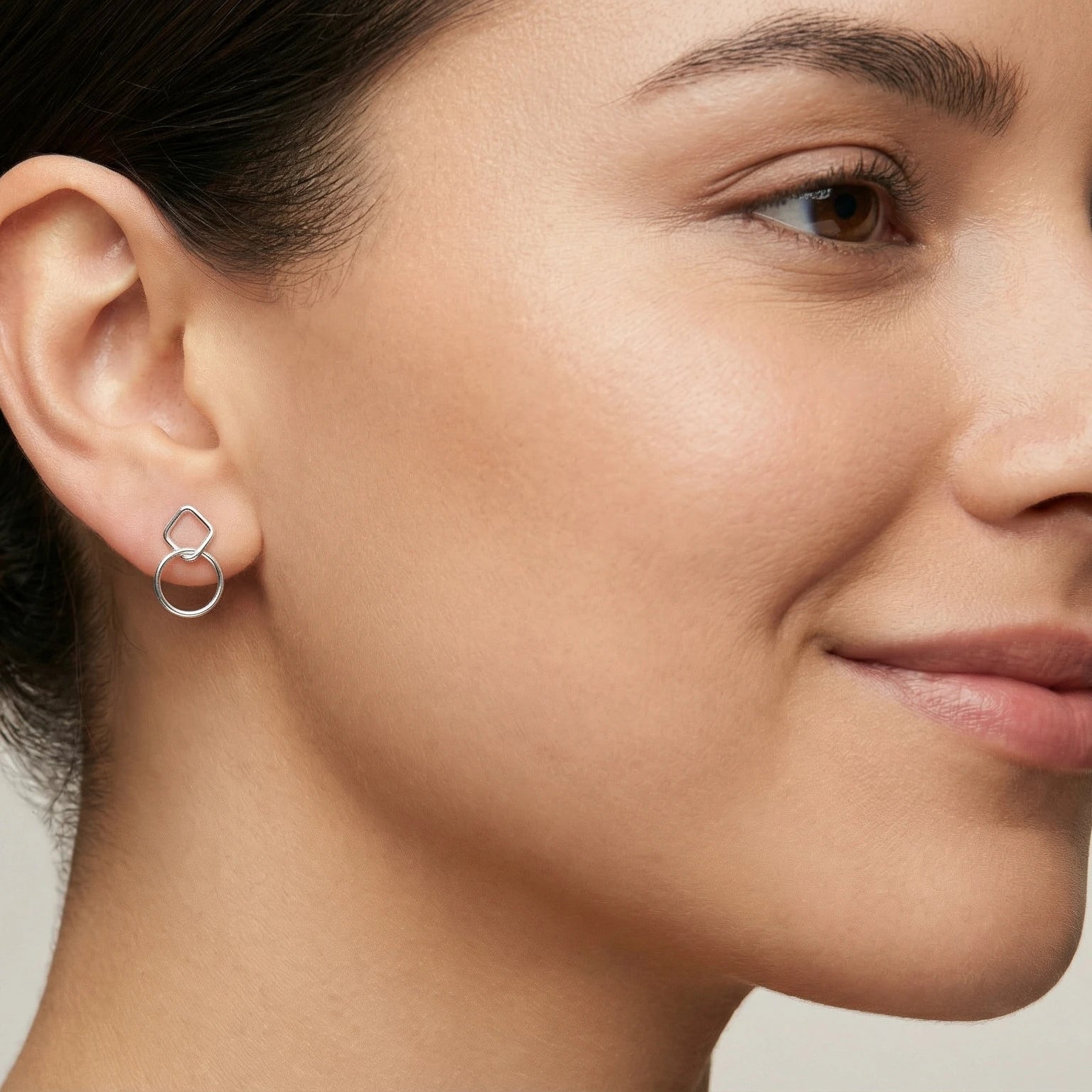 Woman with dark hair wearing stud earring  with a square and a circle intertwined