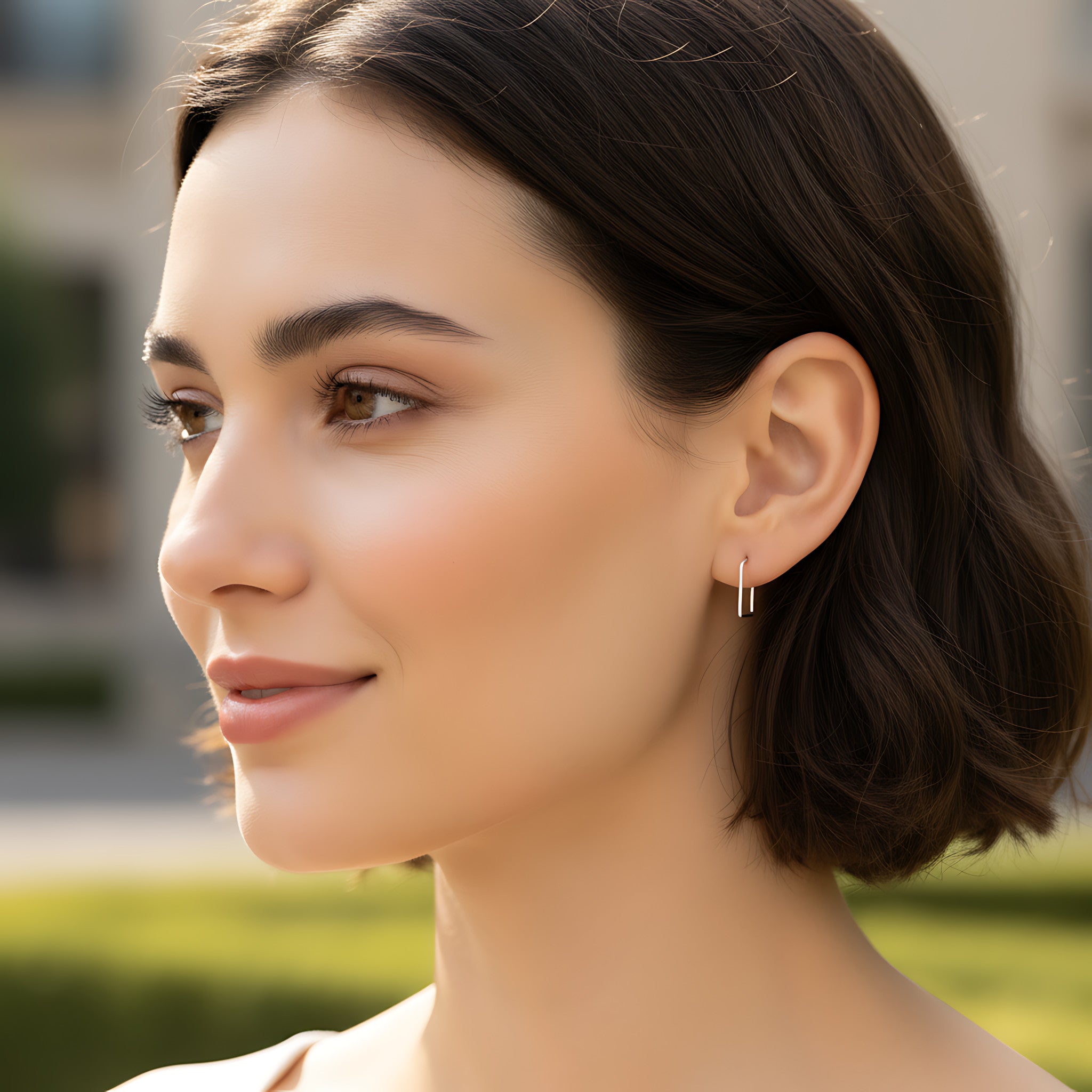 Close-up of a woman wearing a square hoop earring with a blurred outdoor background