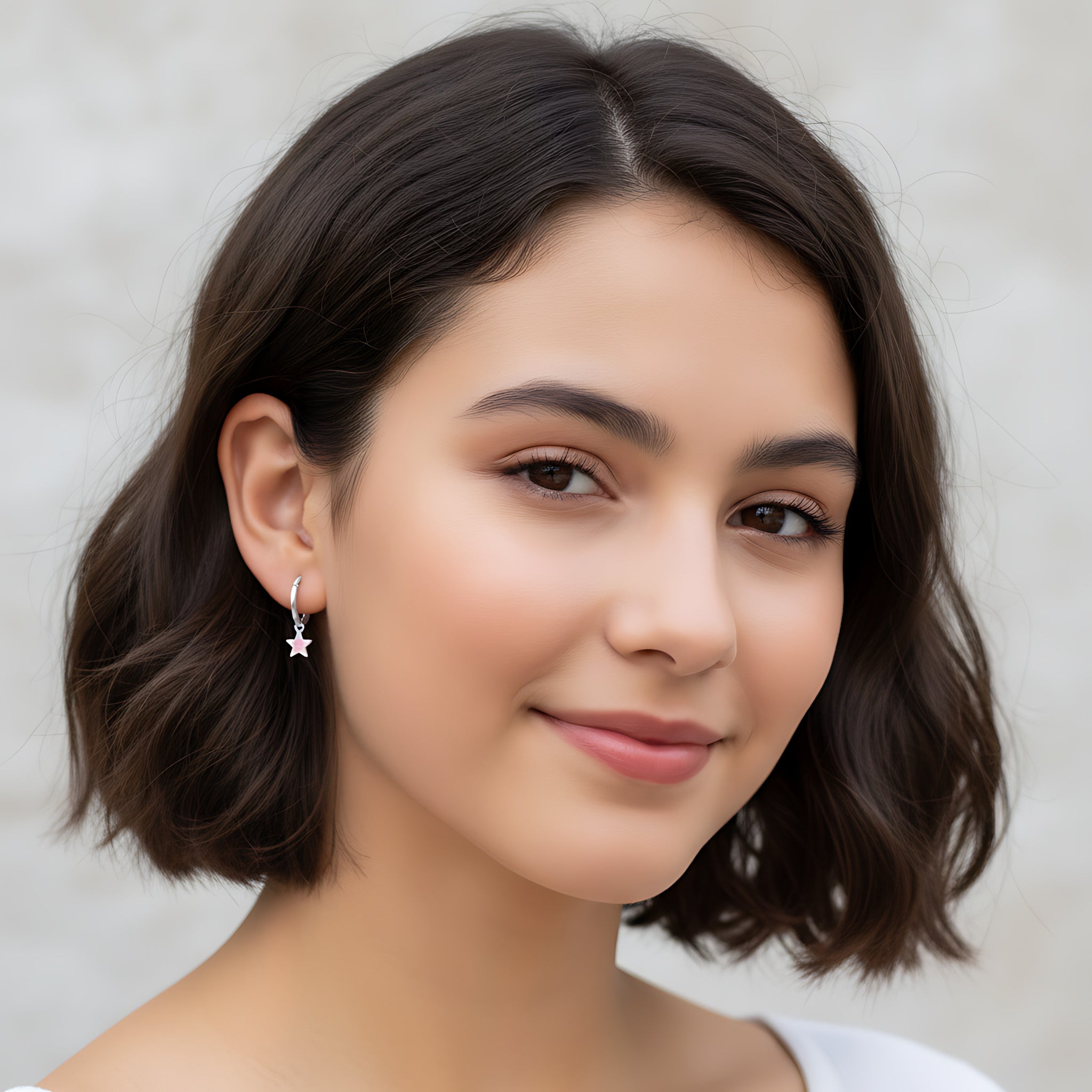 Closeup of a girl wearing a silver hoop earring with a silver star charm on a plain background