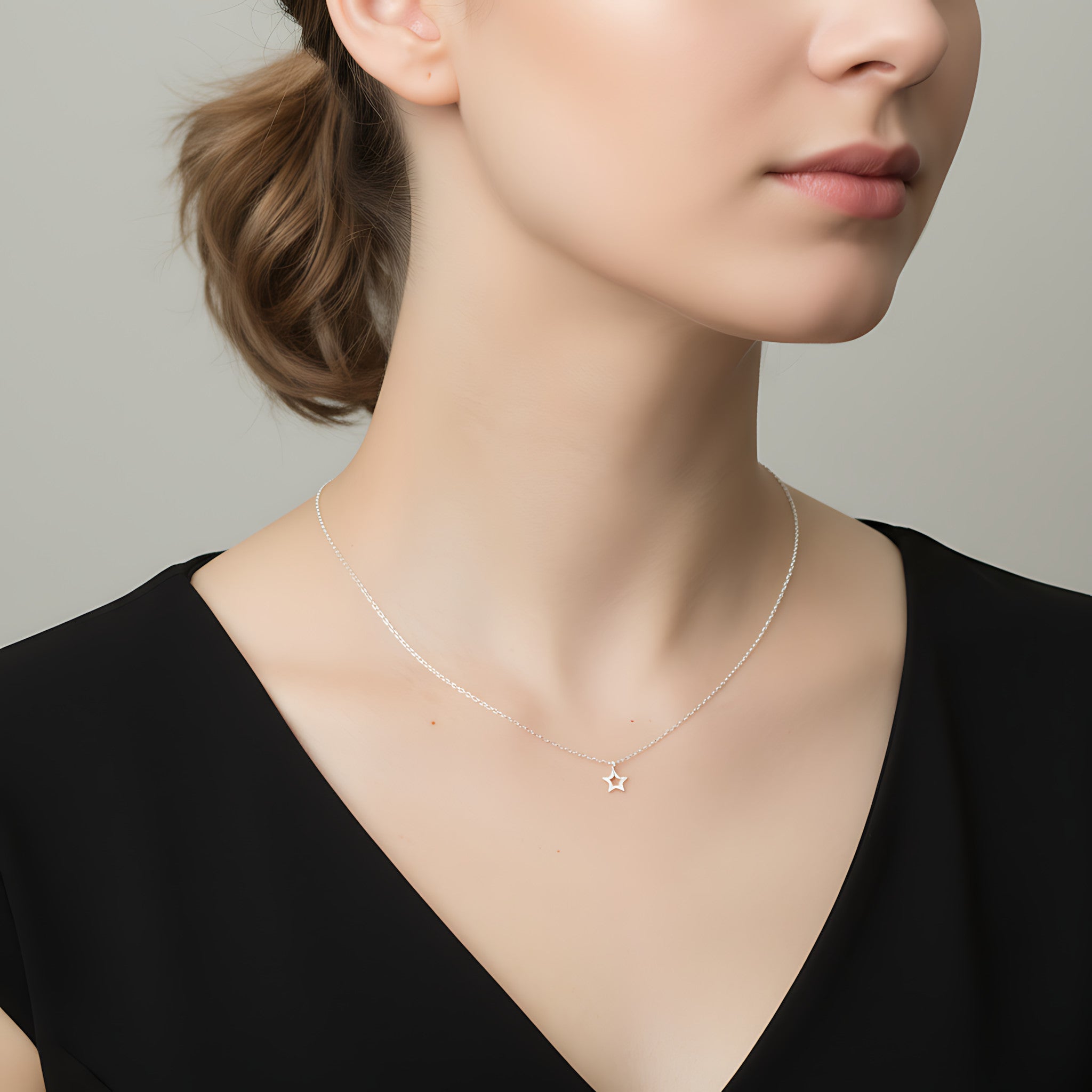Closeup of a female wearing a silver necklace with a small star pendant against a neutral background