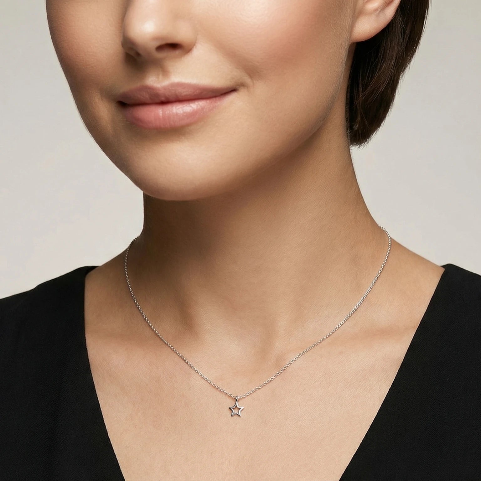 Closeup of a female wearing a silver necklace with a small star pendant against a neutral background