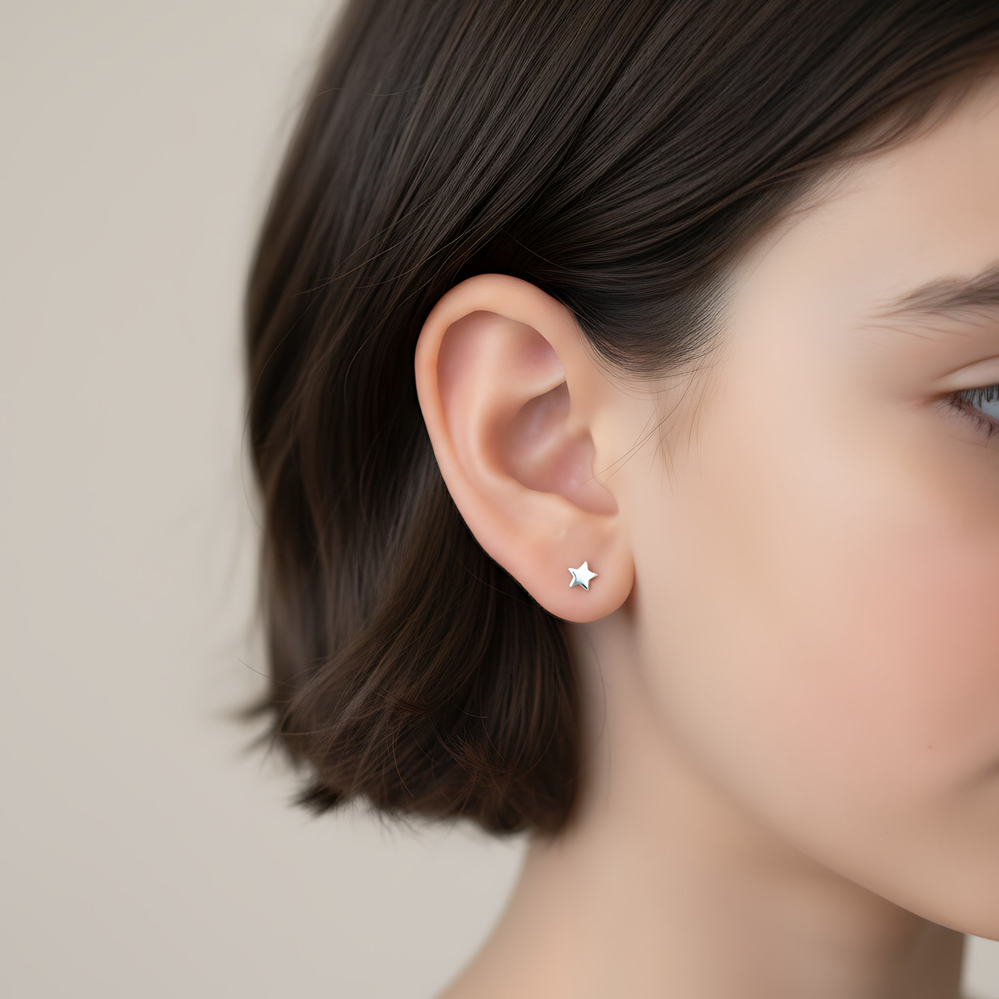Closeup of a girl wearing a silver star shape stud earring on a plain background