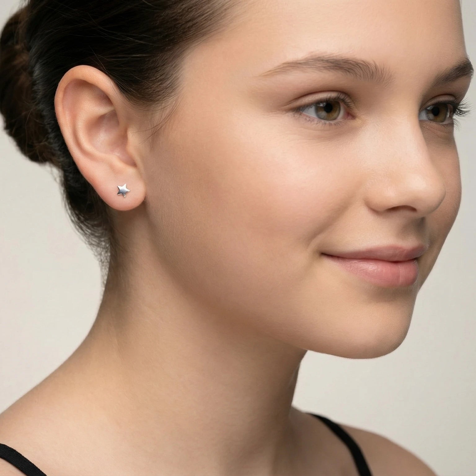 Closeup of a girl wearing a silver star shape stud earring on a plain background