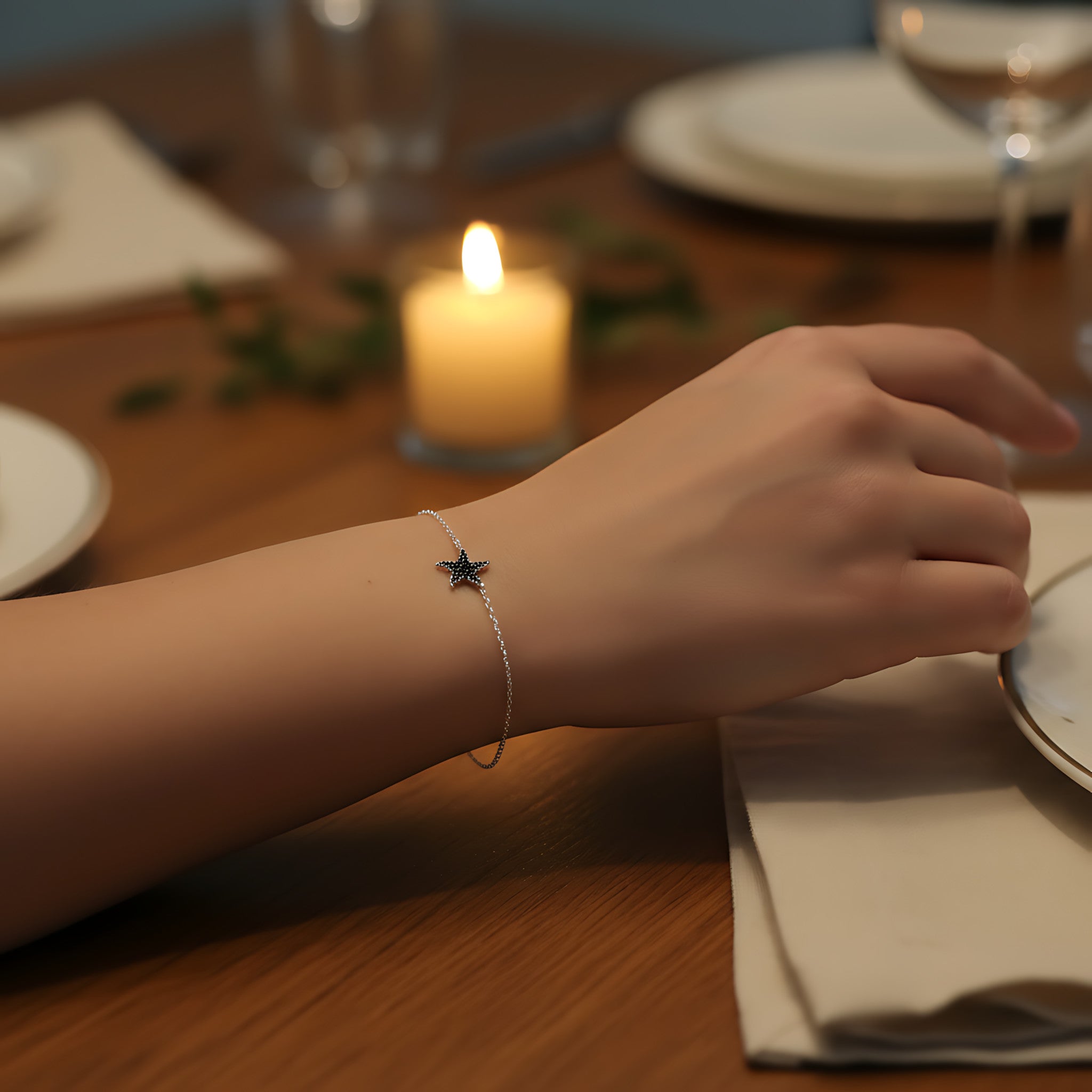 Hand wearing a silver starfish bracelet on a table setting with a candle