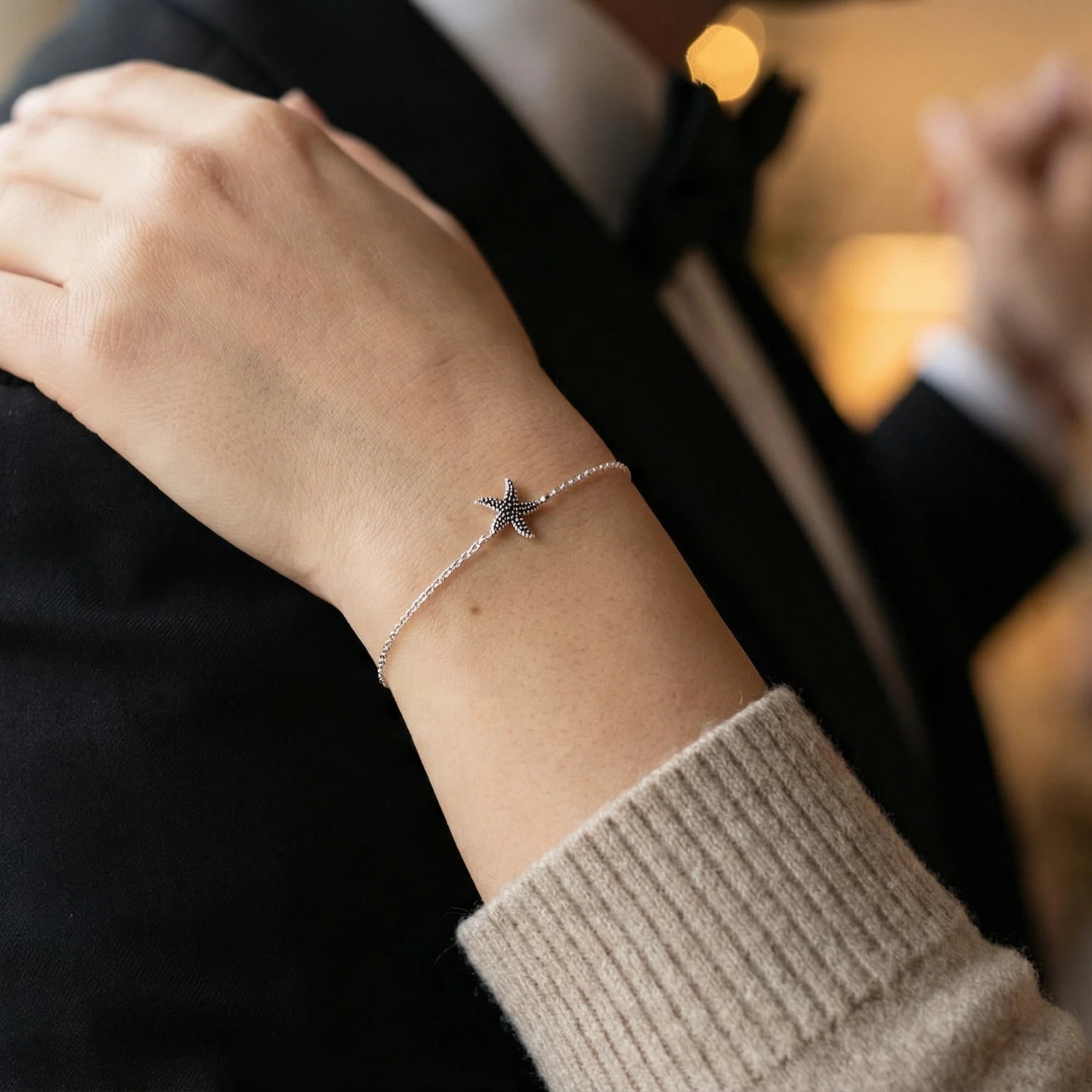 Closeup of a wrist wearing a starfish bracelet rest on a man's shoulder with a blurred background