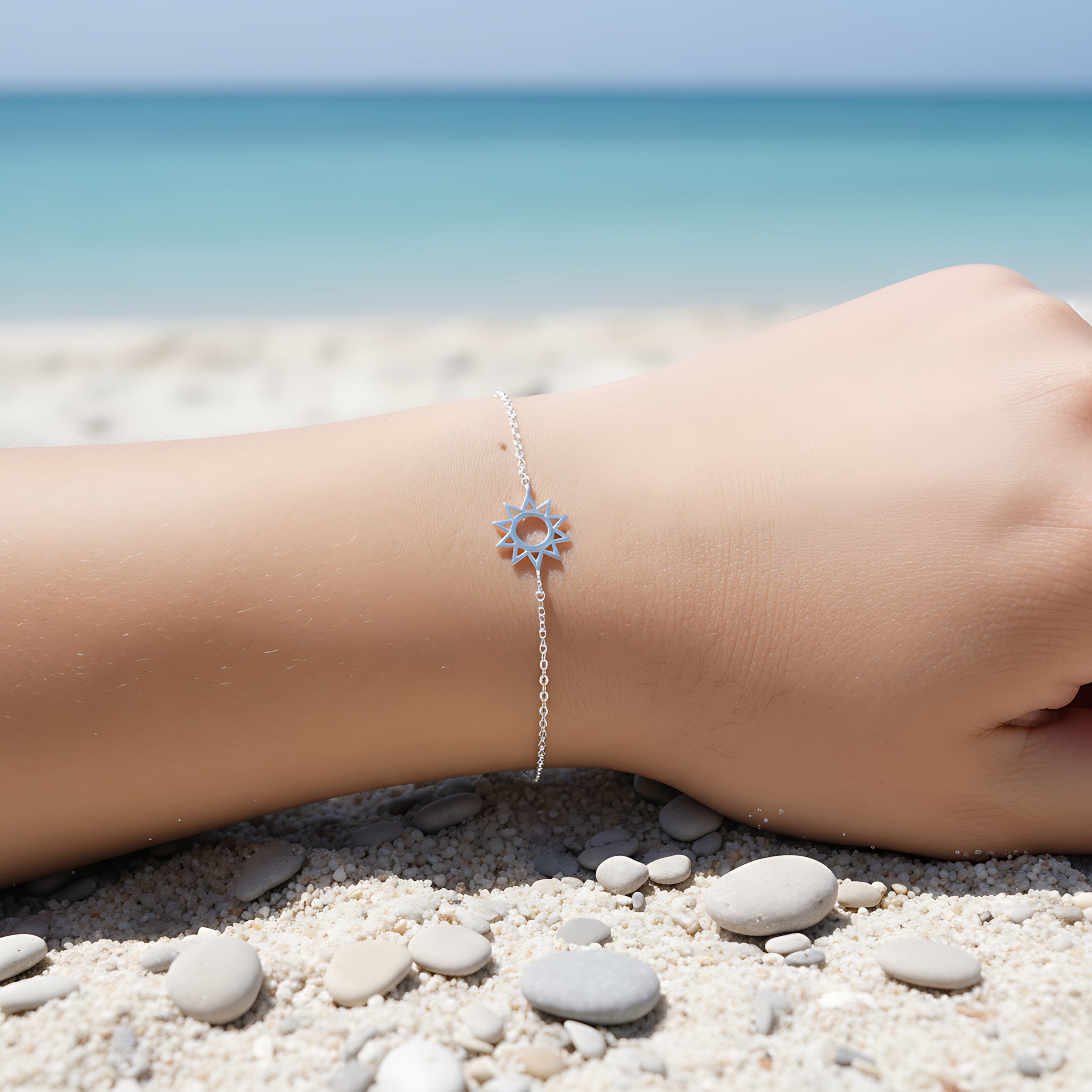 Silver bracelet with a sun charm on a person's wrist by the beach.