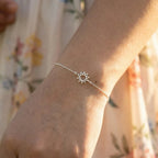 Silver sun-shaped bracelet on a wrist with a blurred floral background