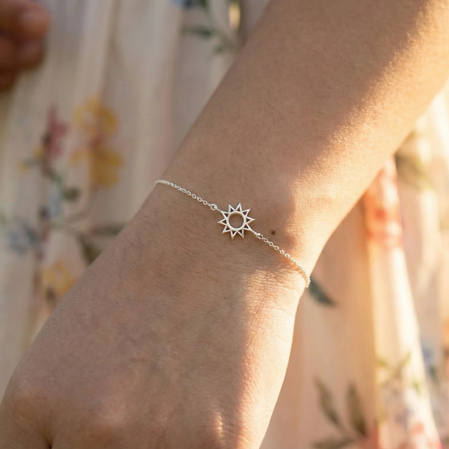 Silver sun-shaped bracelet on a wrist with a blurred floral background