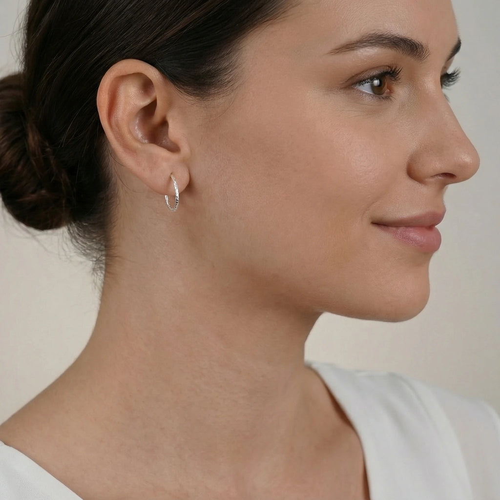Close-up of an ear wearing an elongated silver textured half hoop stud earring with a neutral background