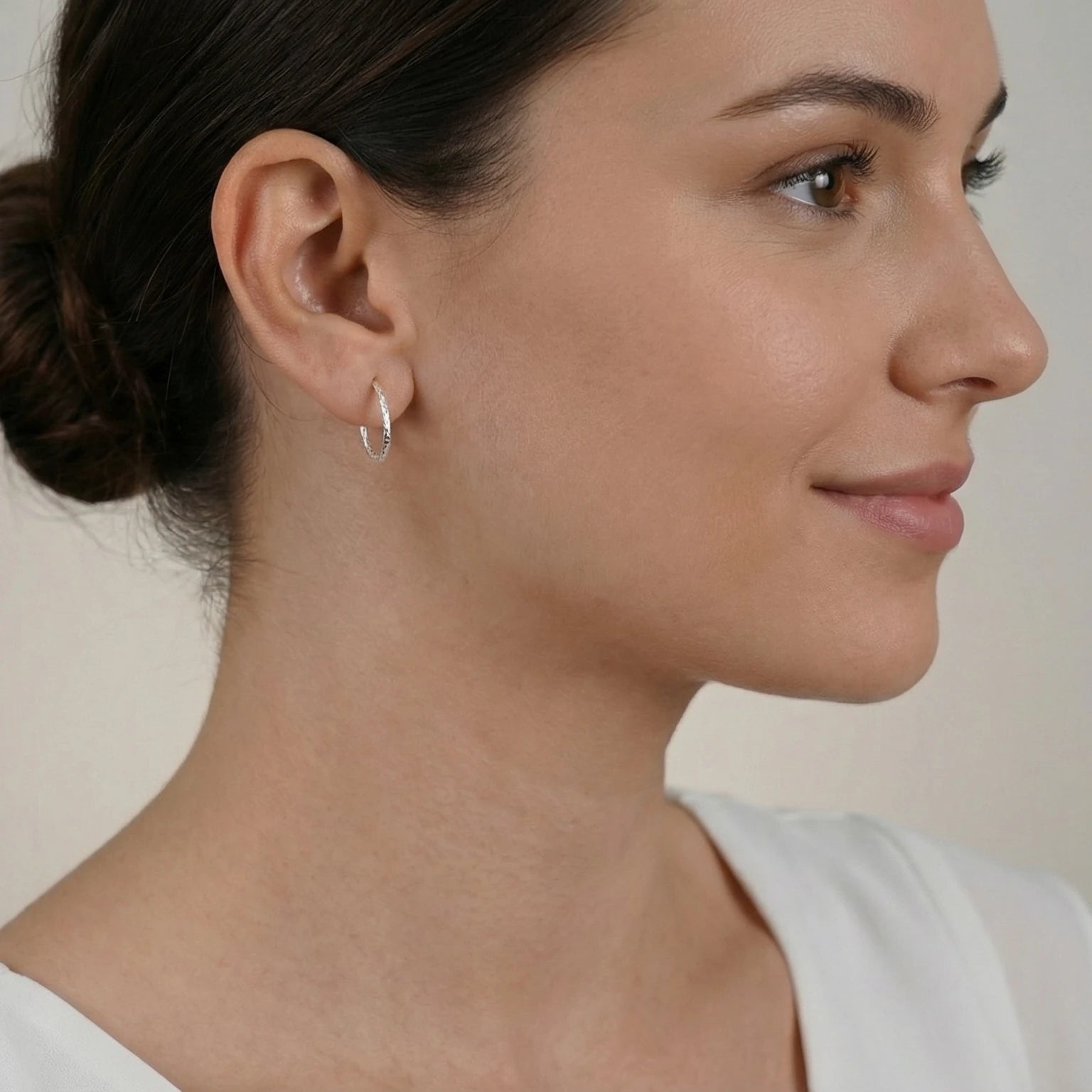 Close-up of an ear wearing an elongated silver textured half hoop stud earring with a neutral background