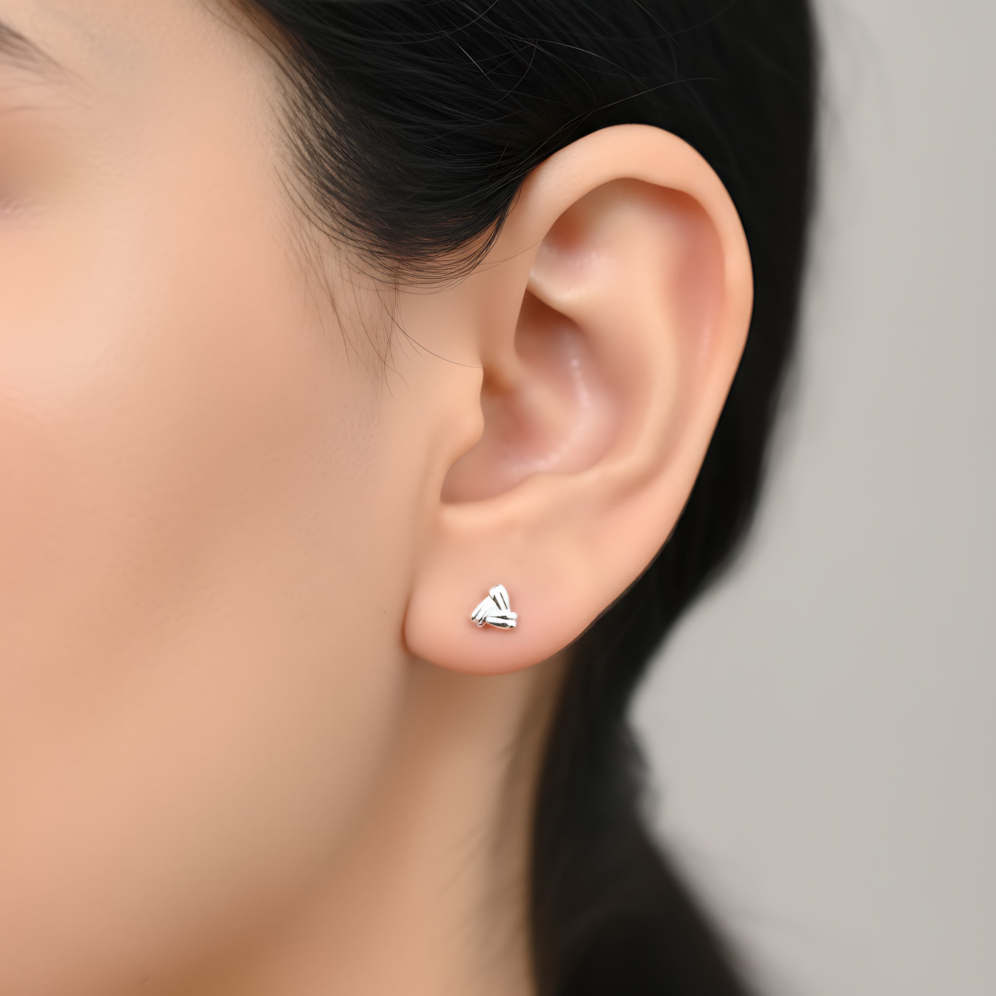 Close-up of an ear wearing a triangular shaped silver stud earring with a gray background