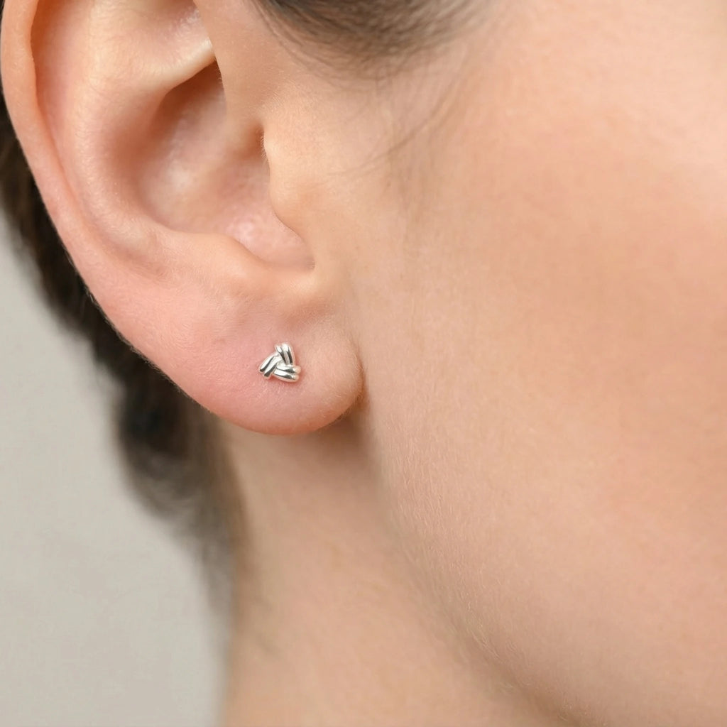 Close-up of an ear wearing a triangular shaped silver stud earring with a gray background