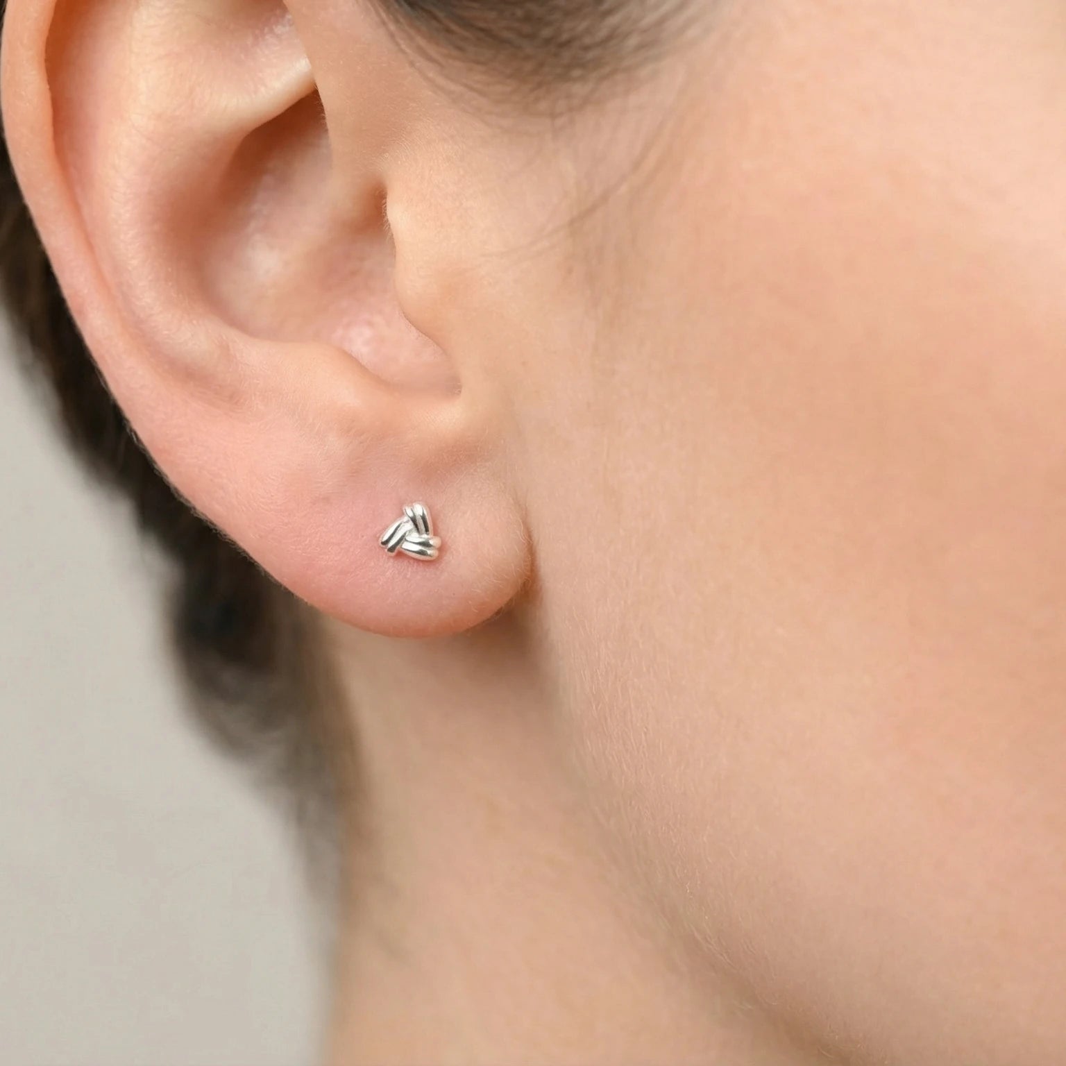 Close-up of an ear wearing a triangular shaped silver stud earring with a gray background