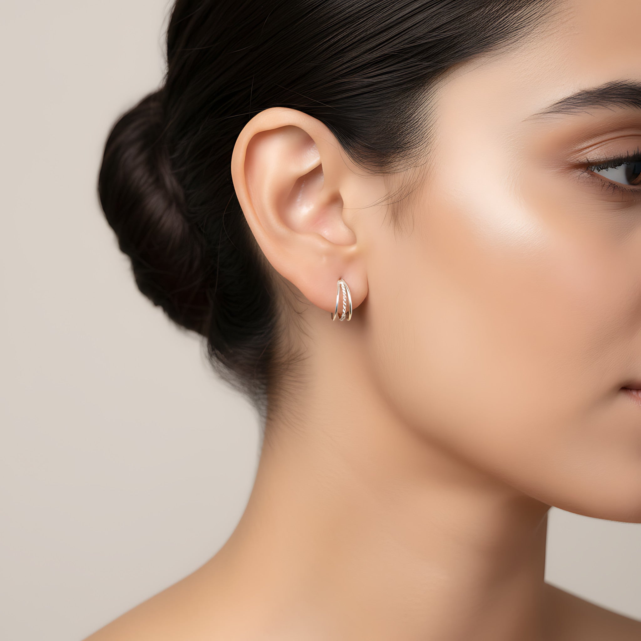Close-up of a woman wearing triple band rope half hoop stud earrings with a neutral background