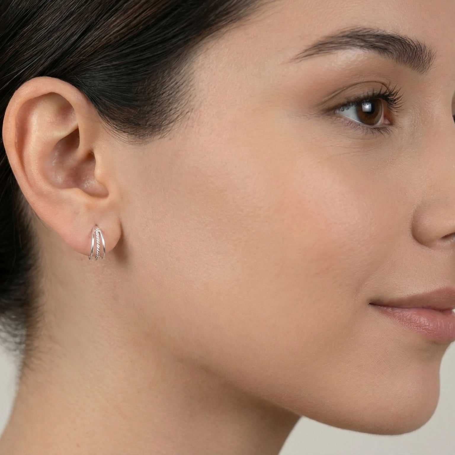 Close-up of a woman wearing triple band rope half hoop stud earrings with a neutral background