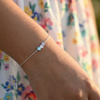 Close-up of a girl's wrist wearing a delicate silver bracelet with 3 colorful daisy flower charms against a floral dress.