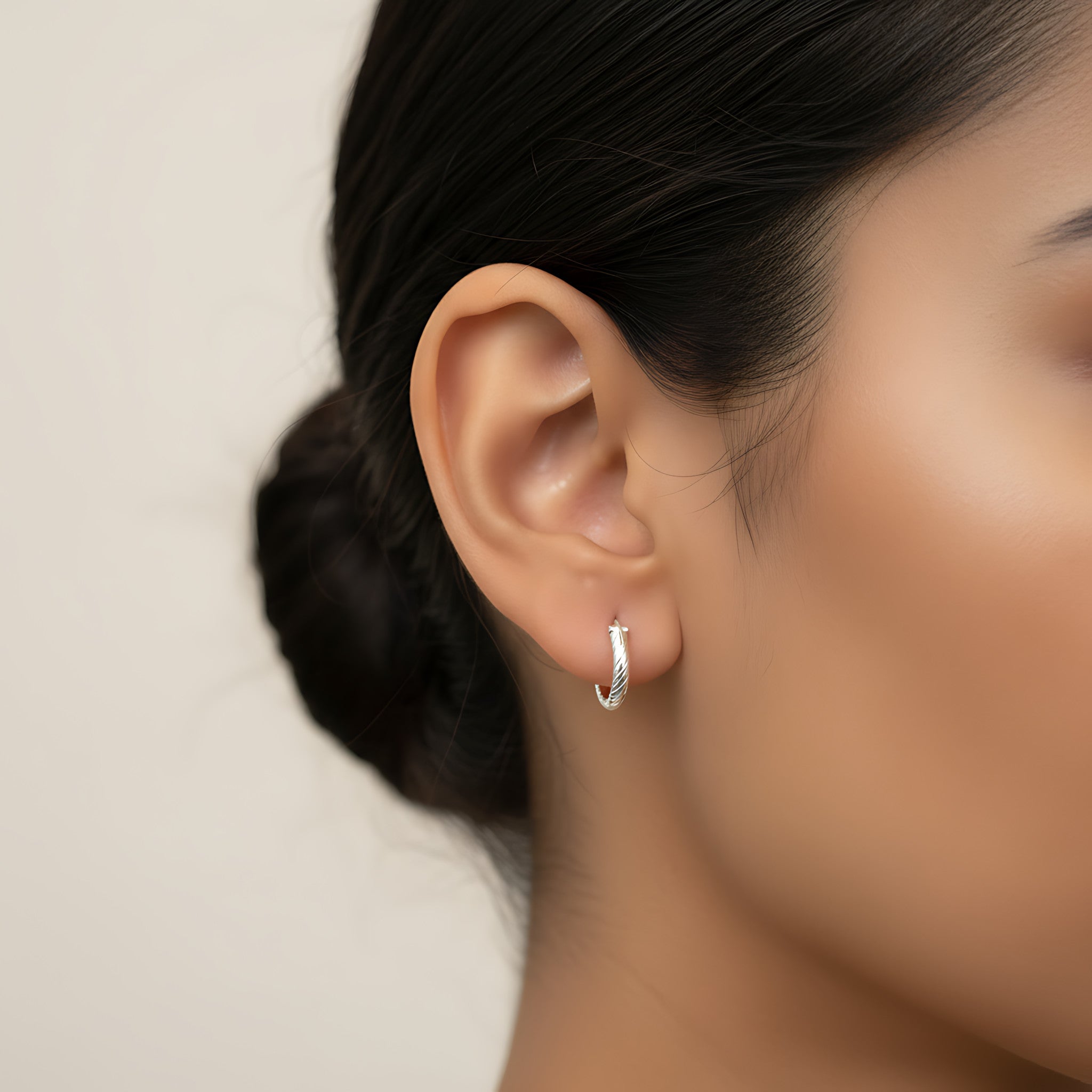 Close-up of an ear wearing a twist textured silver hoop earring with a blurred background