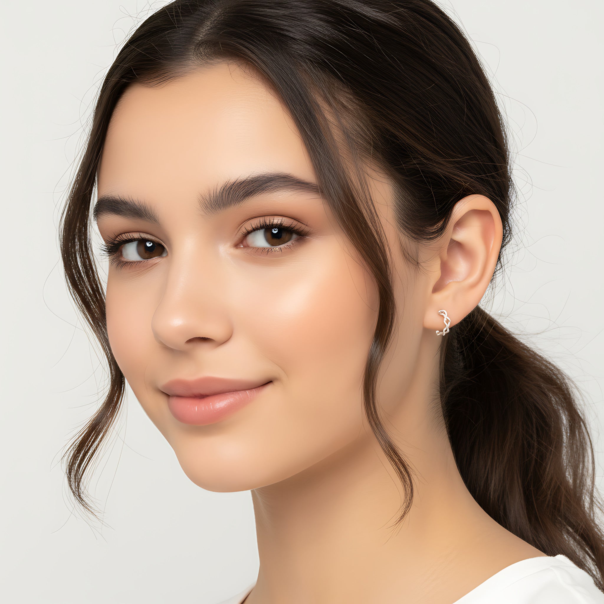 Close-up of a young girl with a ponytail wearing Silver Twisted Half Hoop Stud Earrings against a plain background