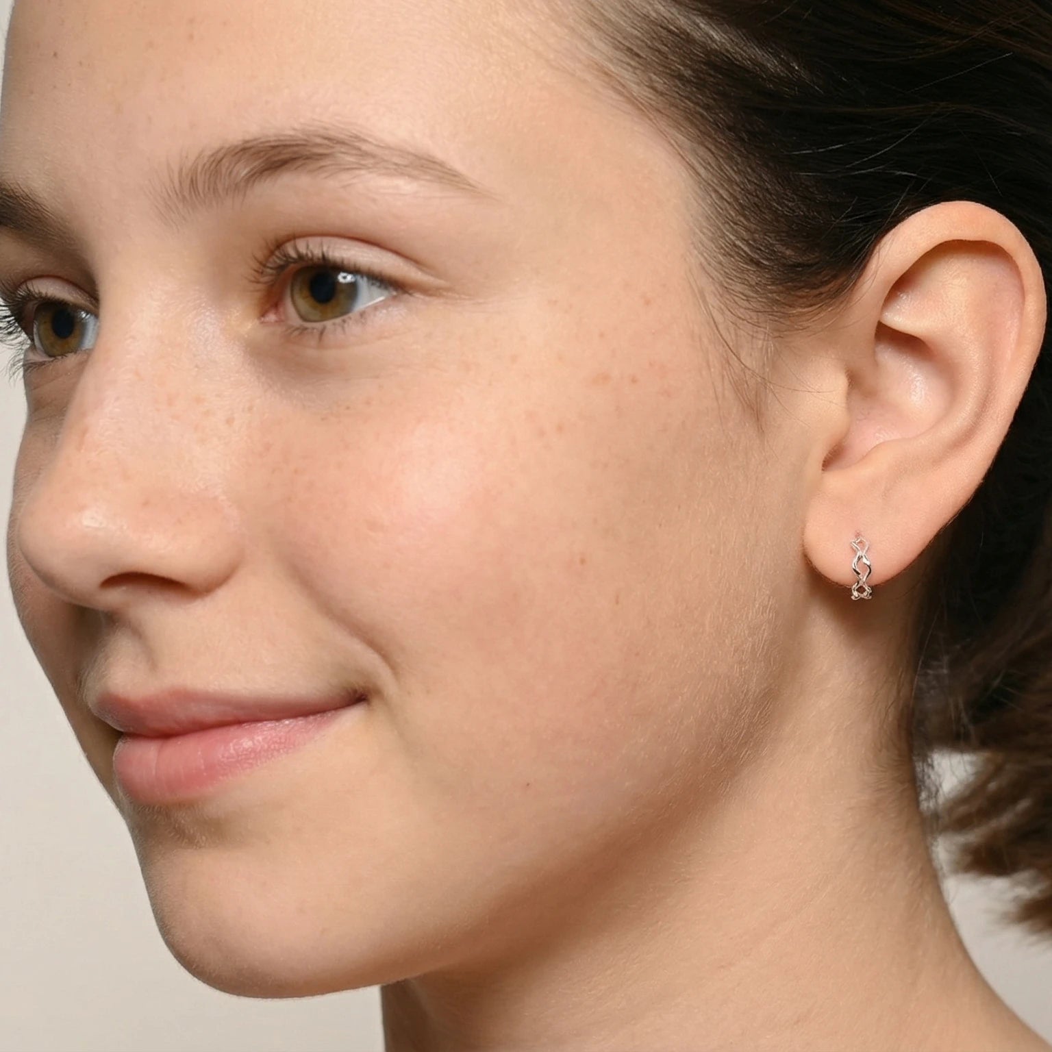 Close-up of a young girl wearing Silver Twisted Half Hoop Stud Earrings against a plain background