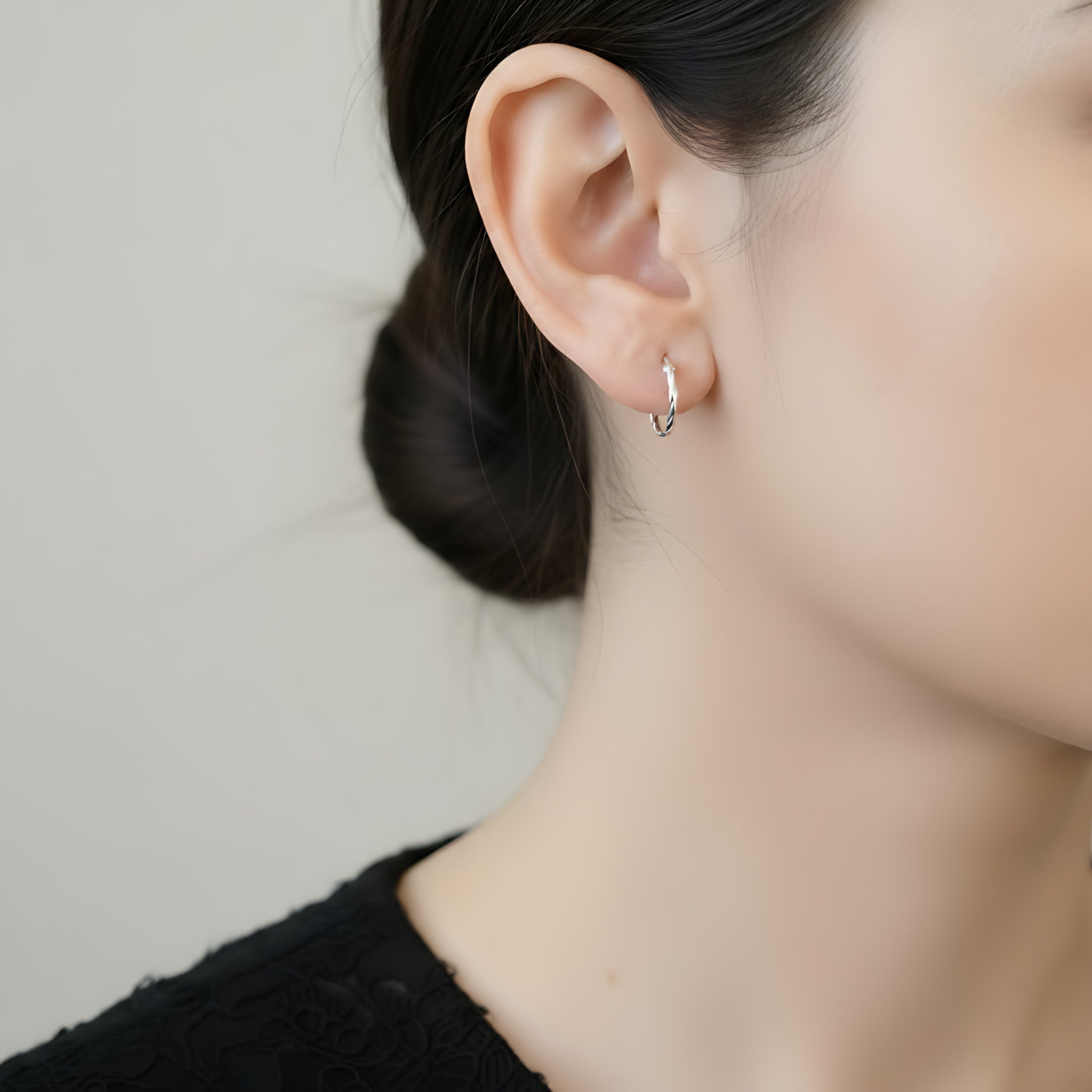 Close-up of a person wearing a twister silver hoop earring with a neutral background