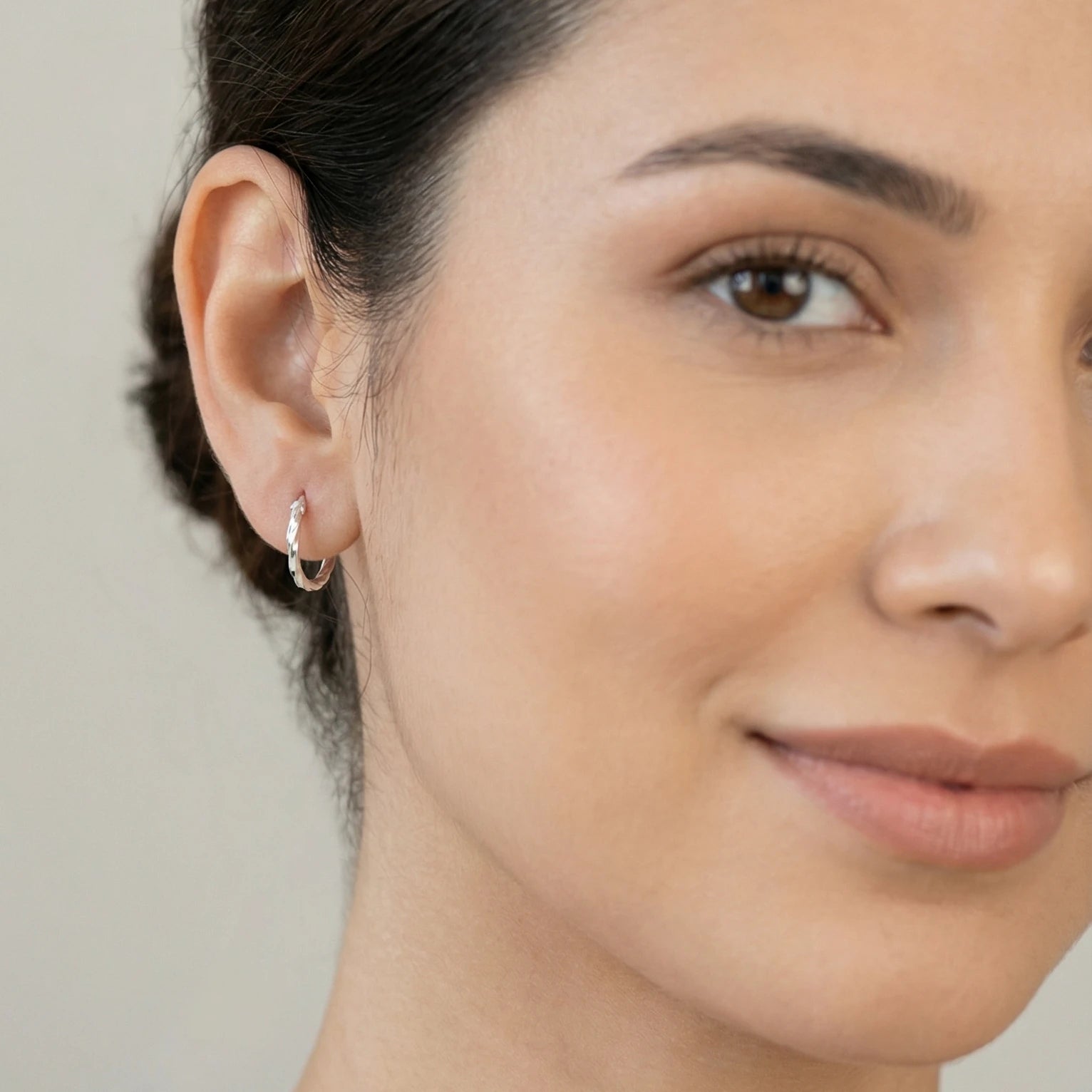 Close-up of a person wearing a twister silver hoop earring with a neutral background