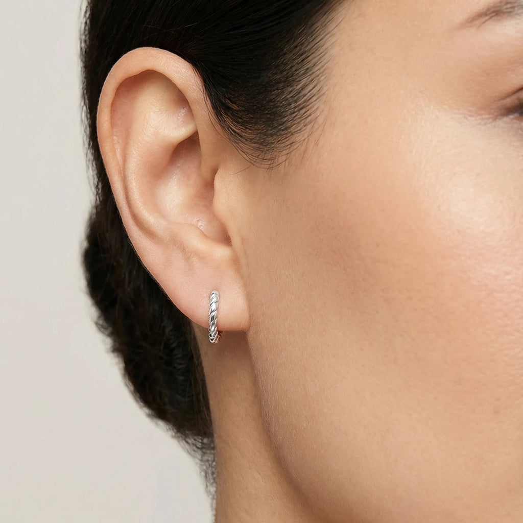 Close-up of a woman wearing a twisted oval silver huggie hoop earring with a neutral background