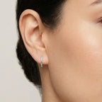 Close-up of a woman wearing a twisted oval silver huggie hoop earring with a neutral background