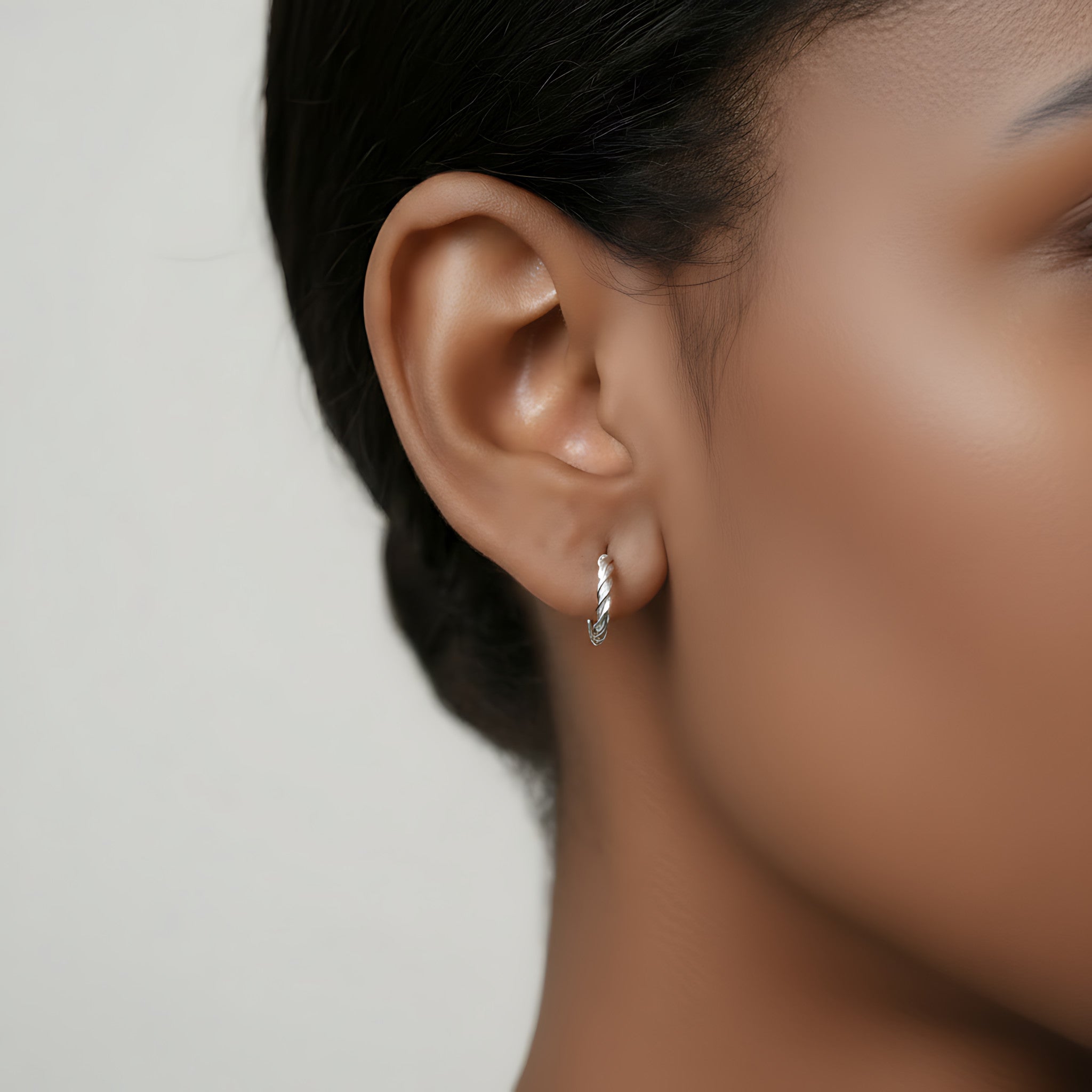 Close-up of an ear wearing a silver twisted rope half hoop stud earring with a blurred background