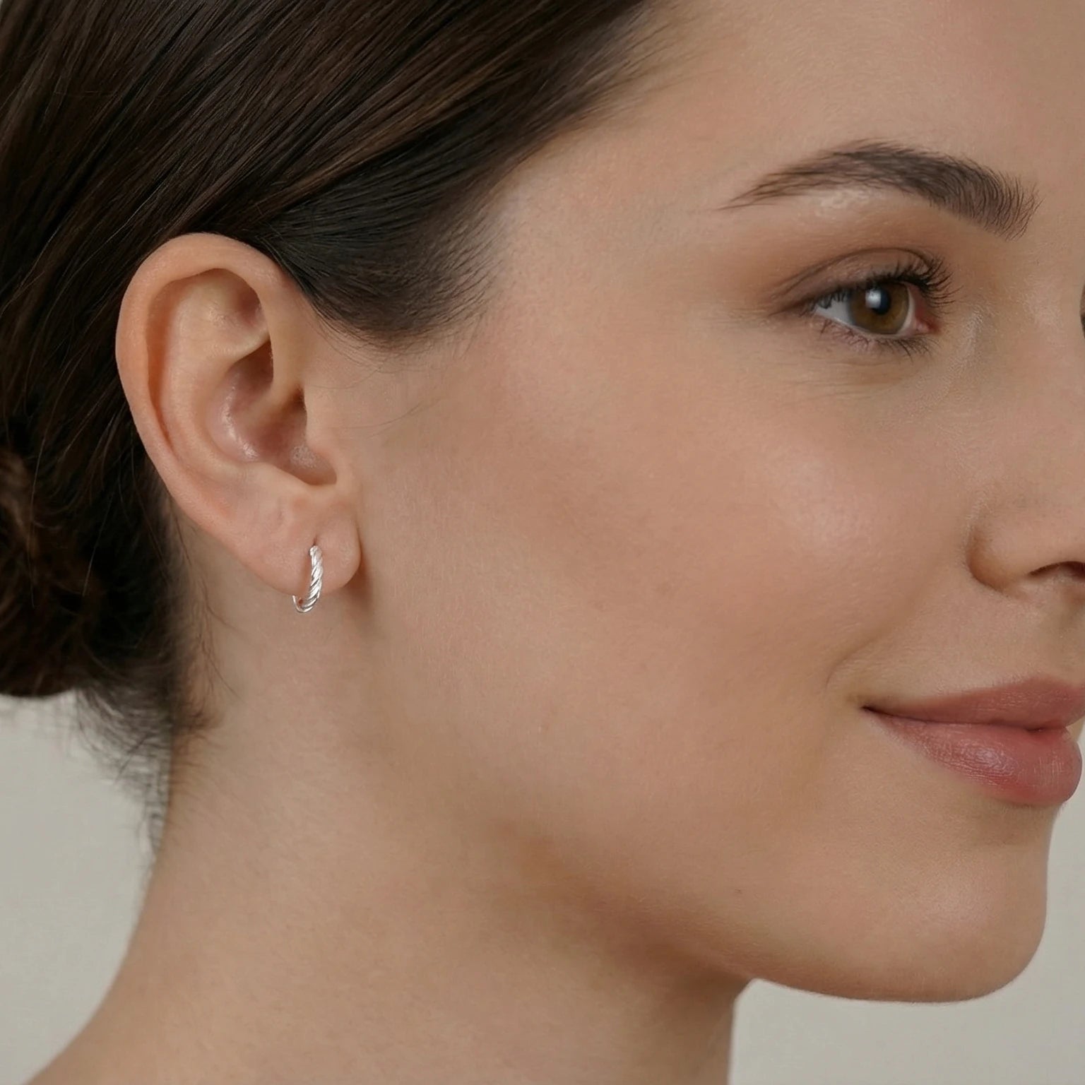 Close-up of an ear wearing a silver twisted rope half hoop stud earring with a neutral background