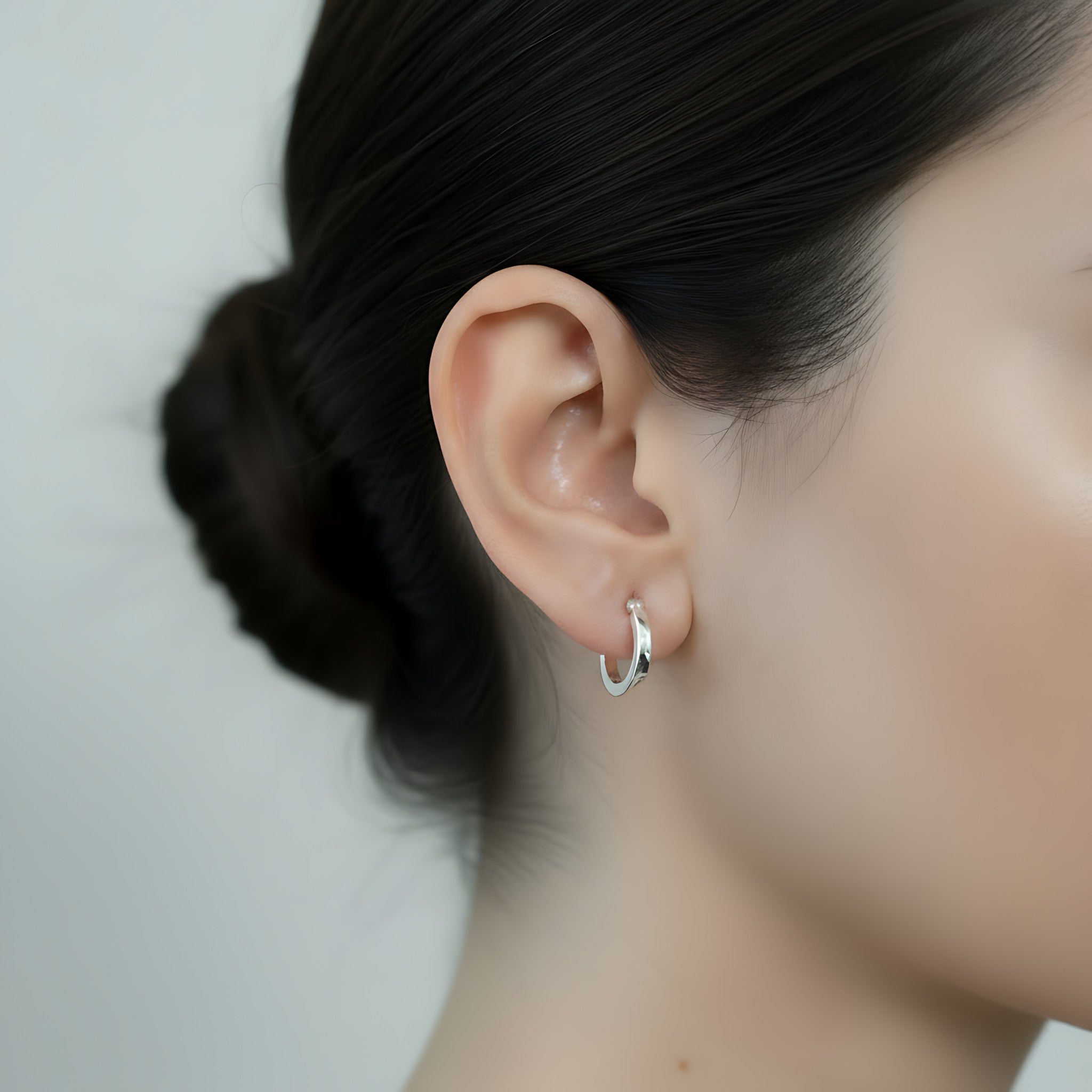 Close-up of an ear wearing a silver French lock hoop earring with a blurred background
