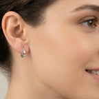 Close-up of an ear wearing a silver French lock hoop earring with a blurred background