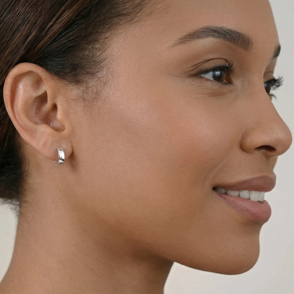 Close-up of a woman wearing a wide band silver hoop earring with ribbed inside on a neutral background