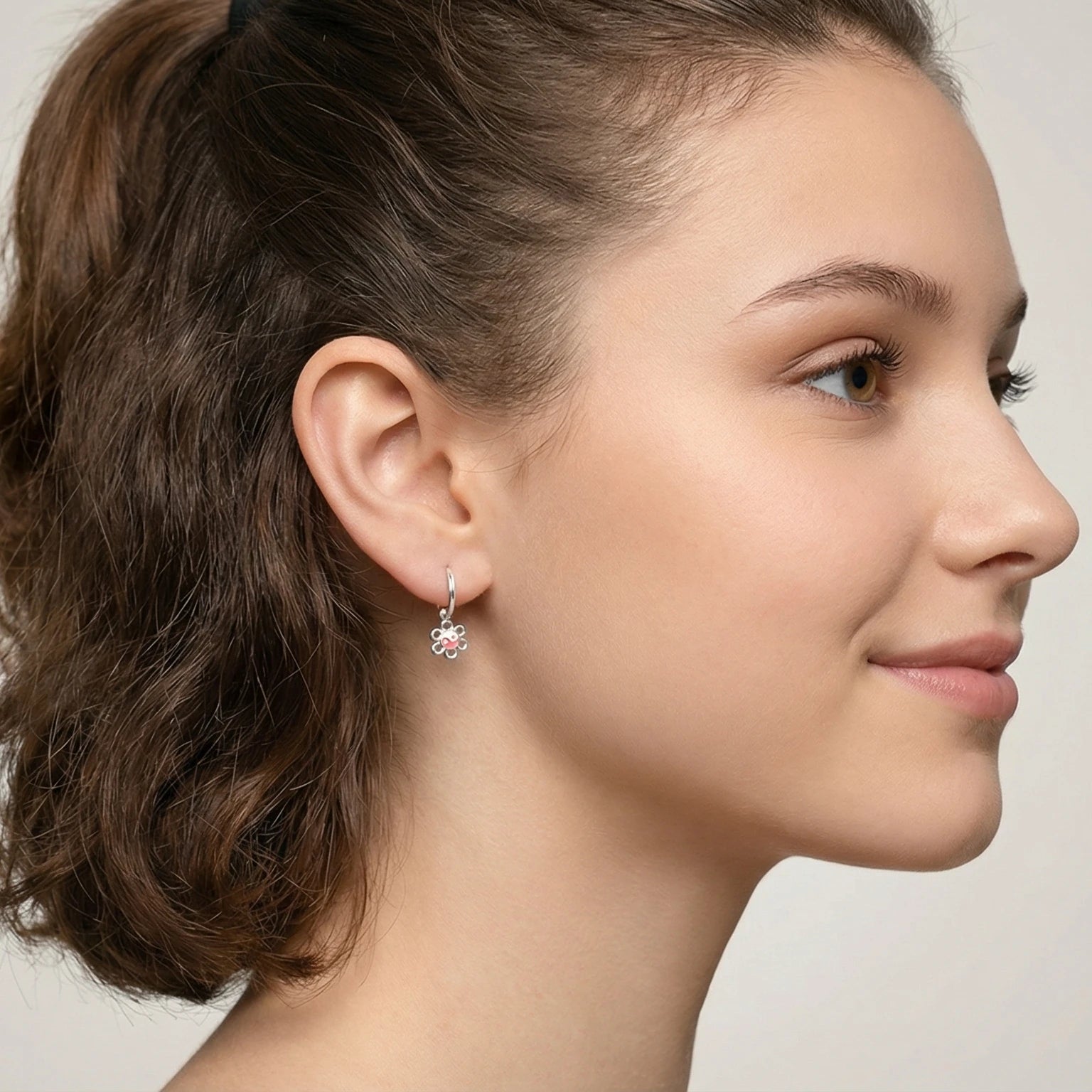 Close-up of a young girl with styled hair and hoop earrings with yin-yang flower charm against a neutral background