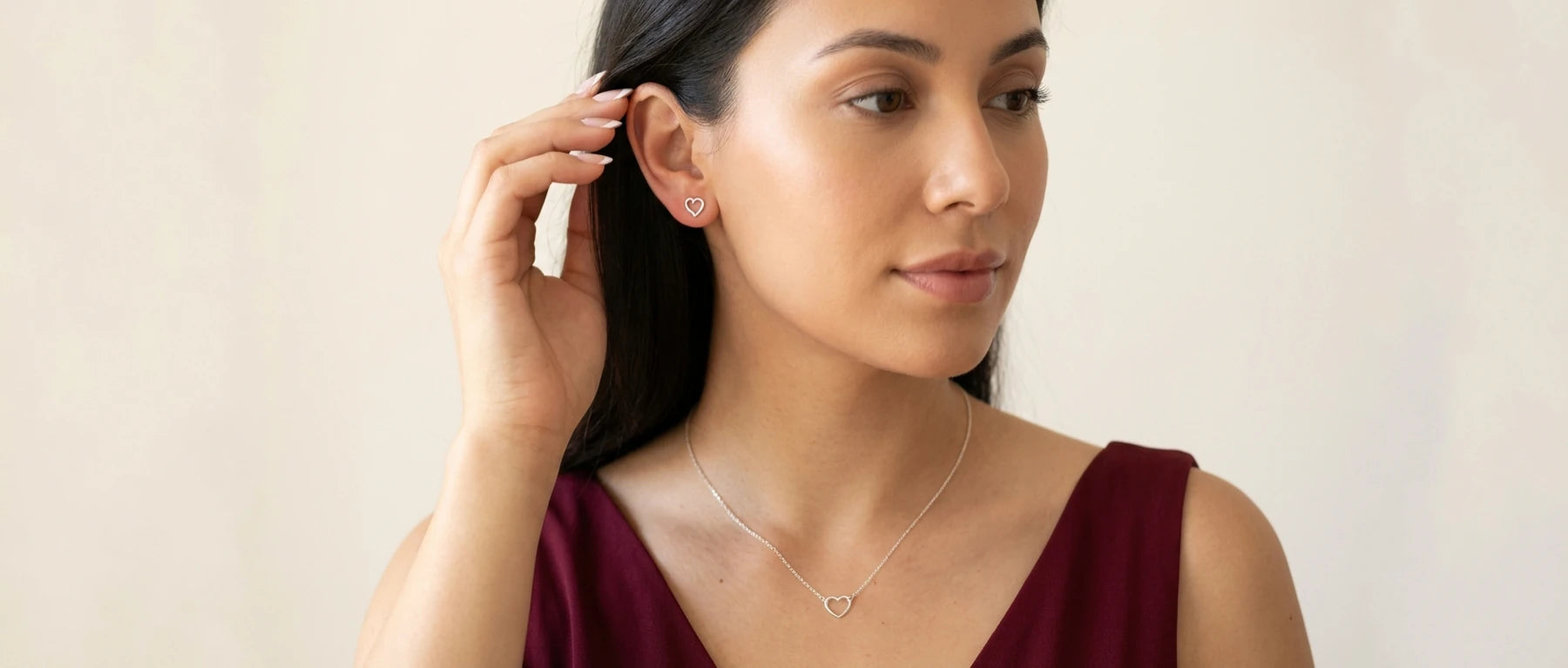 Woman wearing a heart necklace and heart studs against a plain background